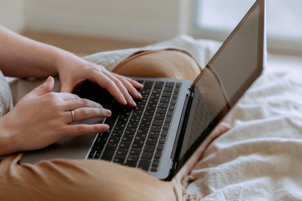 faceless woman using laptop while sitting on bed